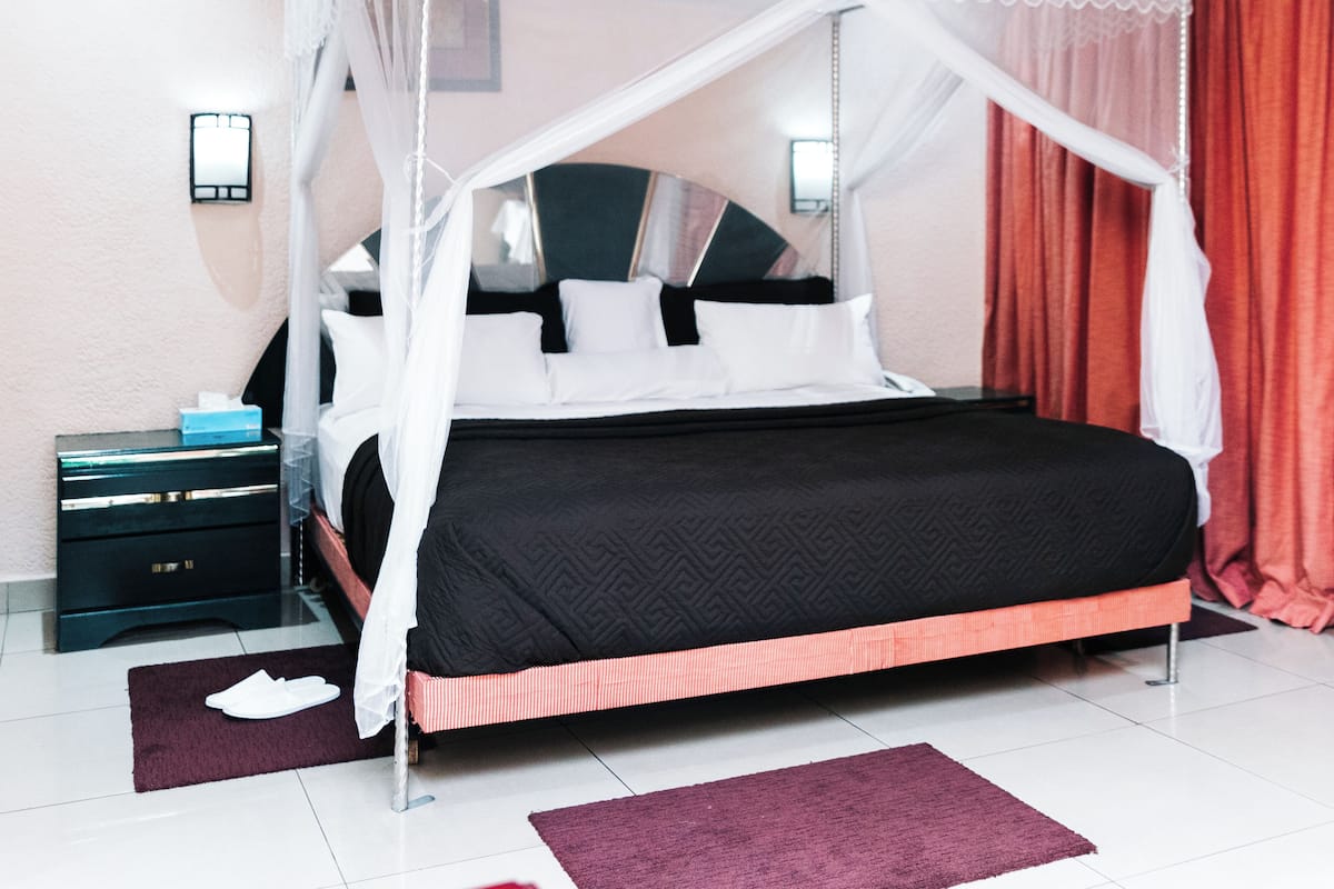 Een hemelbed met een zwart-wit sprei, een nachtkastje met een lamp en een rood gordijn.