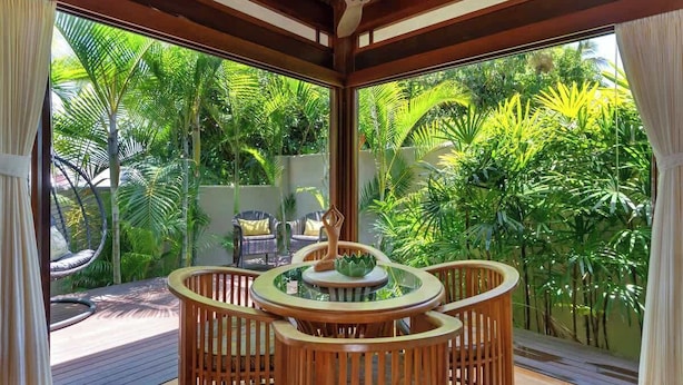 Una habitación con una mesa y sillas de madera, ventanas amplias y vistas a exuberante follaje exterior.