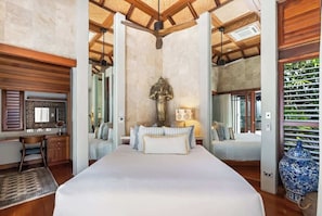 A spacious bedroom with a large bed, a desk, and a chair, a ceiling fan, and a decorative statue.