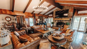 A spacious living room with leather sofas, a stone fireplace, and a large TV mounted on the wall. - Spacious lakeview lodge on Lake Cumberland with WiFi, AC (Seventy Six)