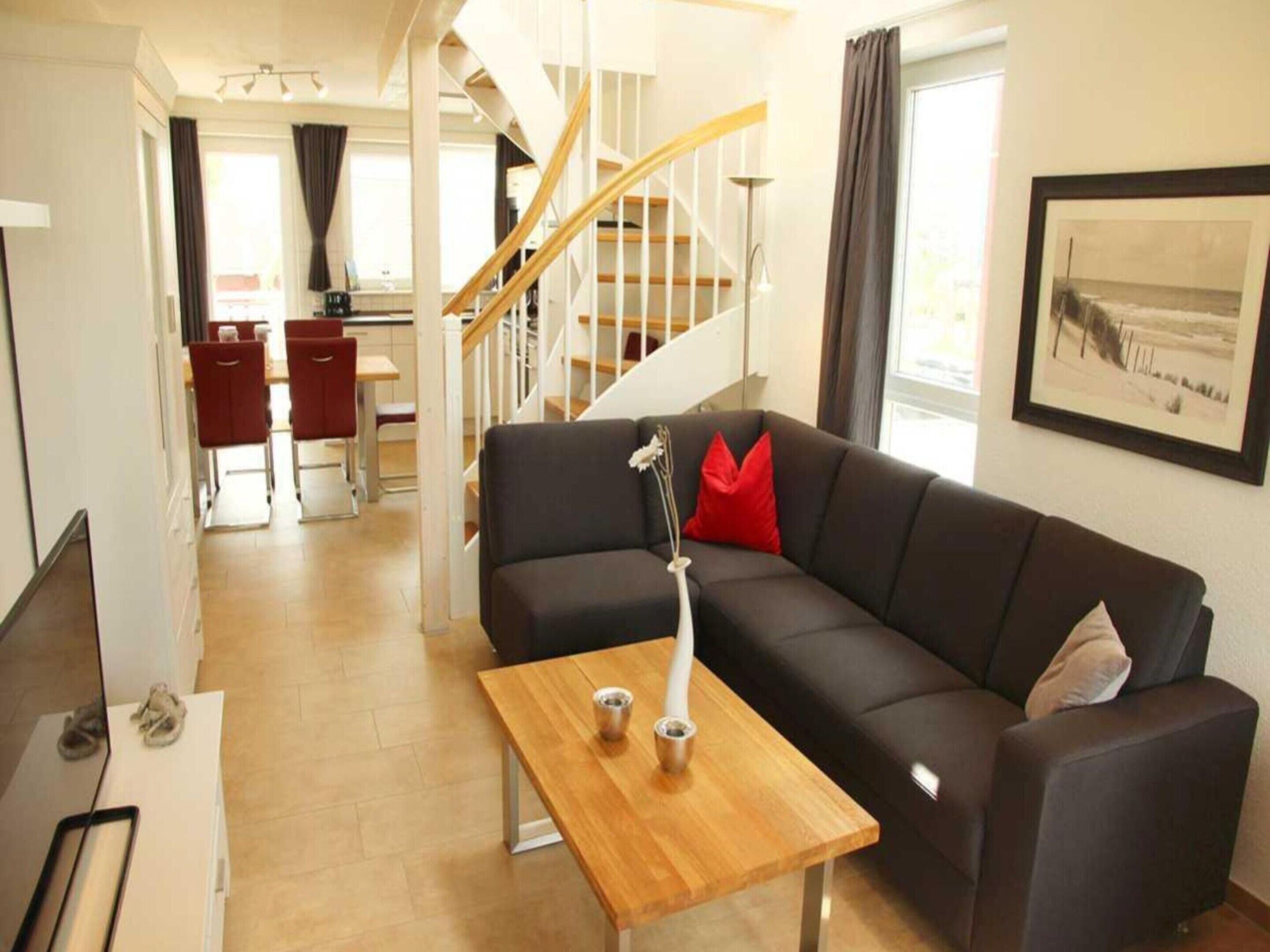 Un salon moderne avec un canapé foncé, une table basse en bois et un escalier menant à un autre niveau.