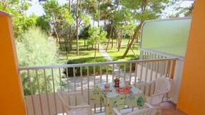 A balcony with a table and chairs, a view of a garden, and a white railing. - Elegant Group Stay Near Caorle (Caorle)