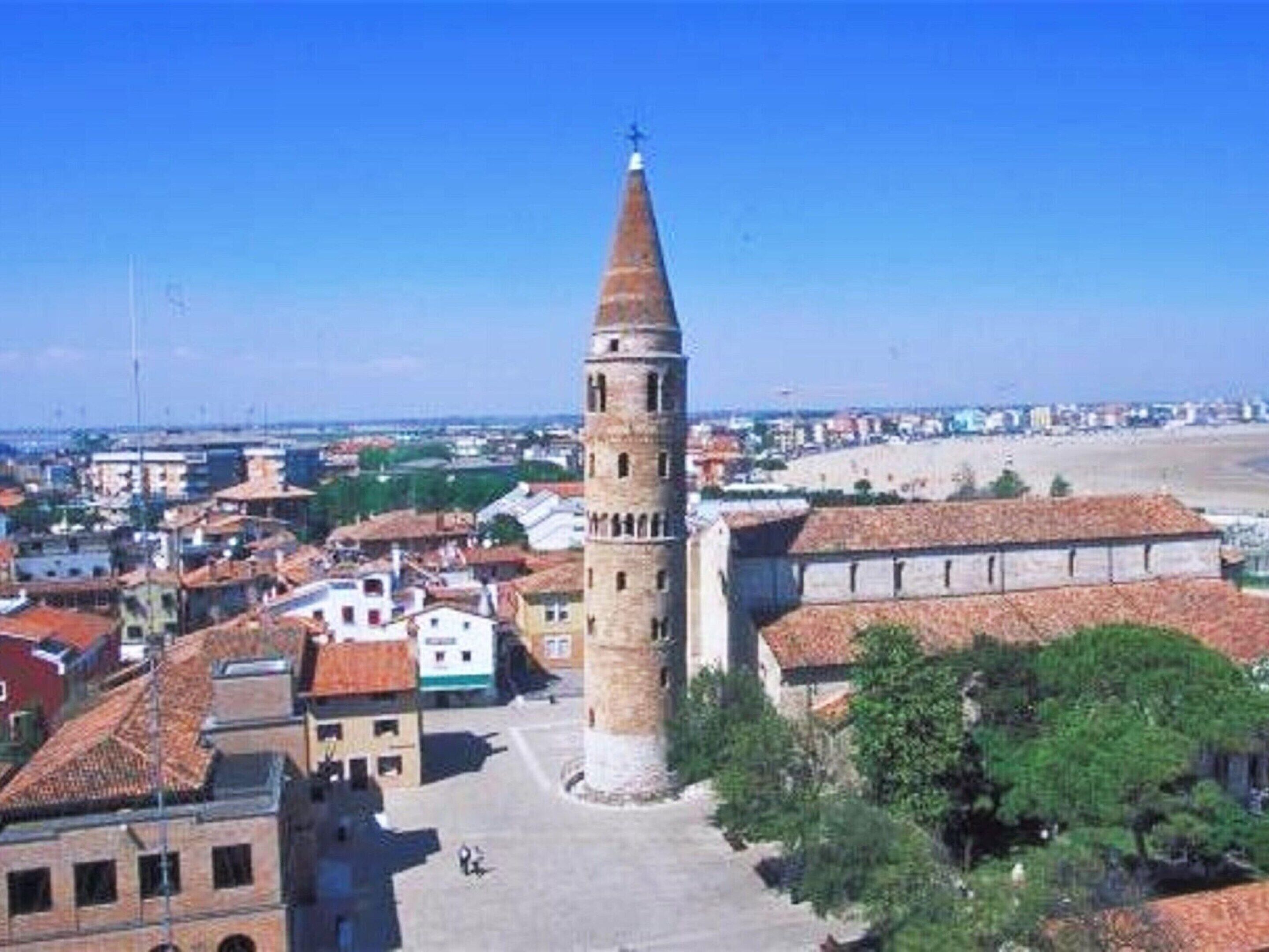 A historic tower with a conical roof, surrounded by a town with red-tiled roofs and a mix of buildings.