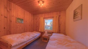 Une chambre dans un chalet en bois, avec deux lits simples, une petite table et une fenêtre avec des rideaux.