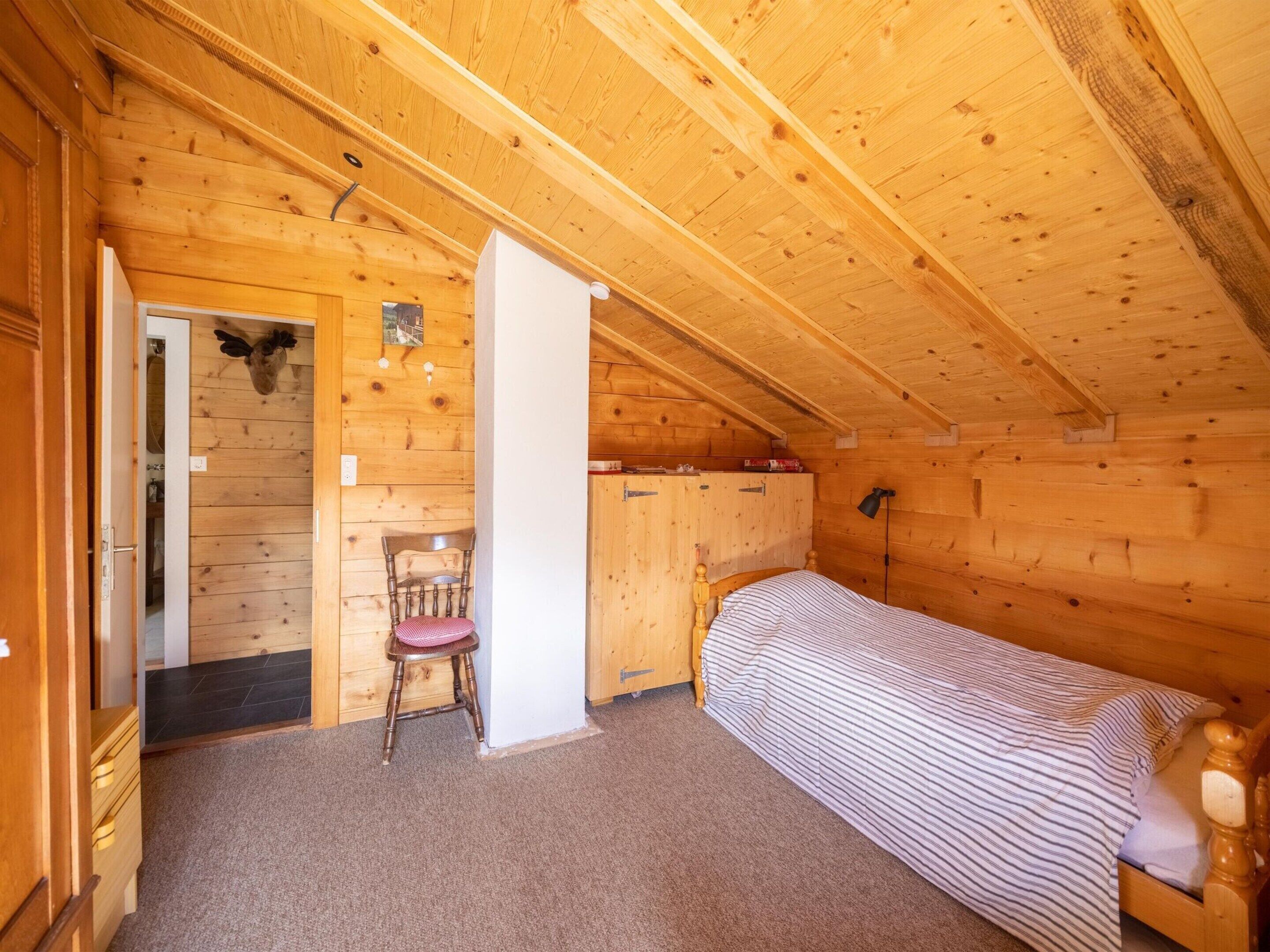 A wooden cabin room with a single bed, a chair, and a small table.