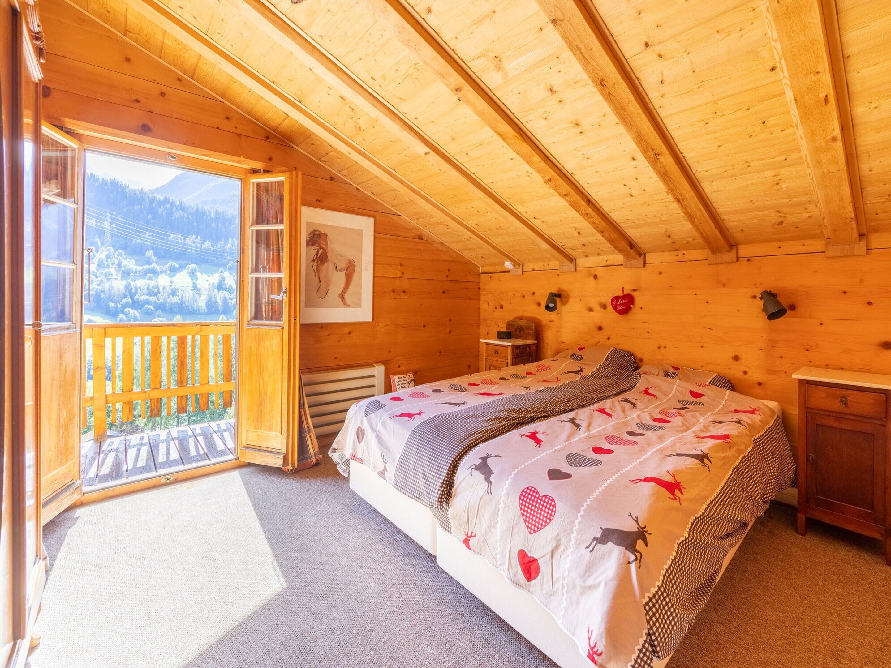 A wooden cabin bedroom with a bed, a nightstand, a dresser, and a window overlooking a snowy landscape.