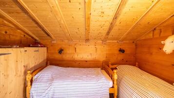 A wooden cabin room with two beds, a wooden ceiling, and a sheep head decoration.