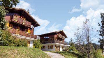Eine Holzchalet mit Balkonen, einem Kiesweg und einem Bergpanorama im Hintergrund.