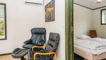A room with a bed, a chair, a small table, an air conditioning unit, and a framed picture on the wall.