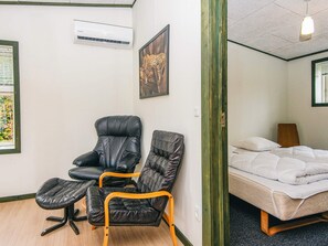 Et værelse med en seng, en stol, et lille bord, en aircondition og et billede i ramme på væggen.