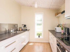 A compact kitchen with a window, white cabinets, a microwave, and a coffee maker. - 4 Star Holiday Home in Hovborg (Hovborg)