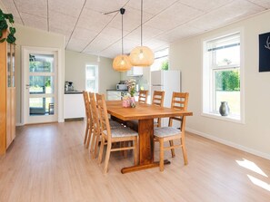 A dining area with a wooden table and chairs, a kitchen in the background, and a view of greenery outside. - 4 Star Holiday Home in Hovborg (Hovborg)
