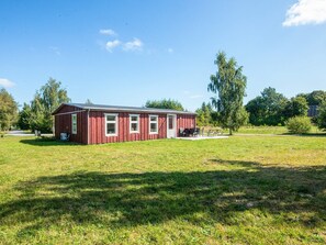 A red wooden building with a flat roof, a door, and windows, situated in a grassy field with trees in the background. - 4 Star Holiday Home in Hovborg (Hovborg)