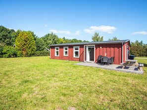En rød træbygning med terrasse, dør og vindue.