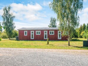 En rød bygning med grusvej og et lille træ foran.
