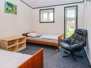 A dormitory room with a single bed, a wooden desk, a black chair, and two windows with blinds. - 4 Star Holiday Home in Hovborg (Hovborg)