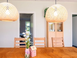 A dining area with a wooden table, two chairs, a vase with flowers, and a small house-shaped object. - 4 Star Holiday Home in Hovborg (Hovborg)