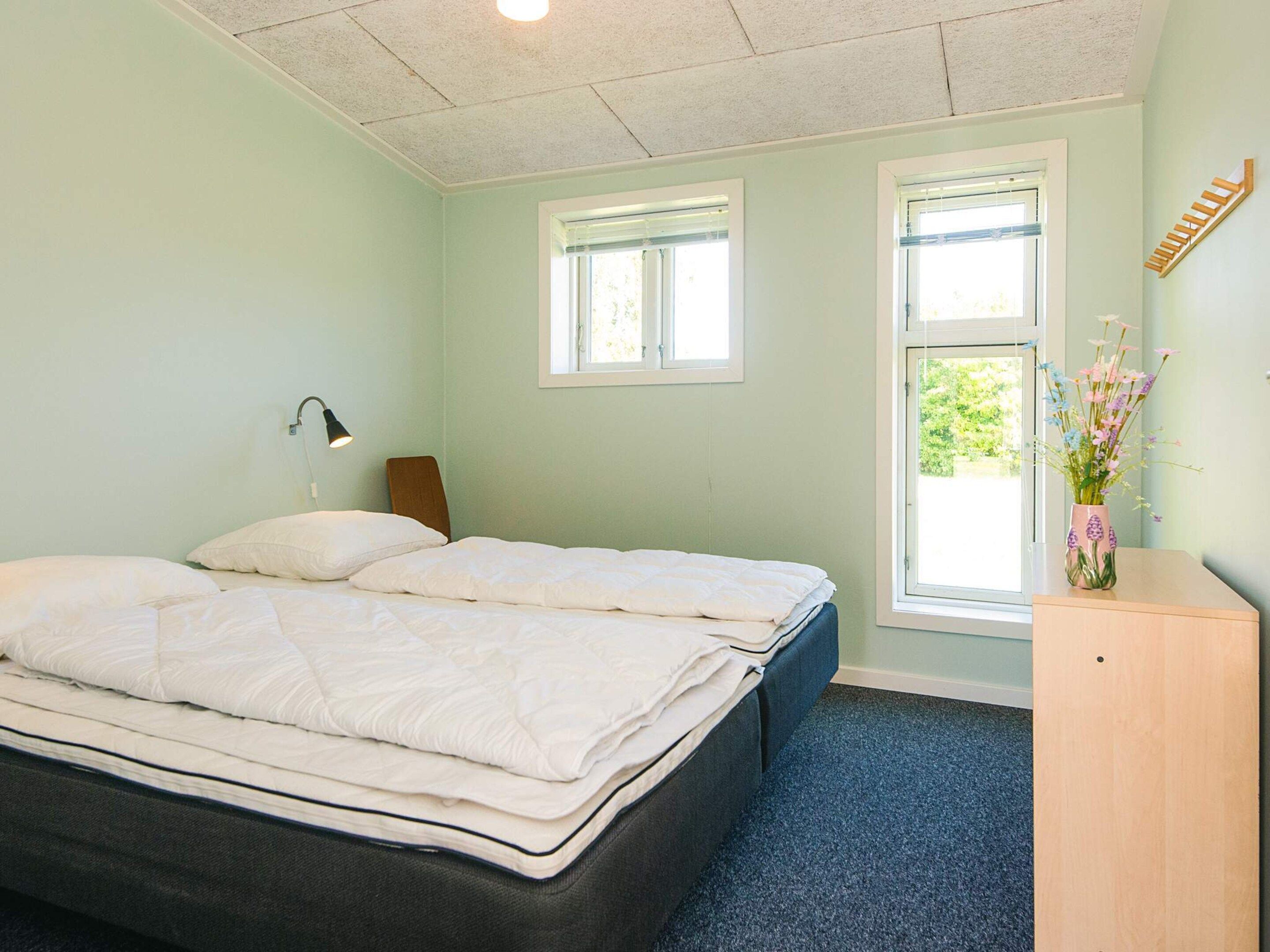 A bedroom with a bed, two windows, a desk, a chair, and a lamp.