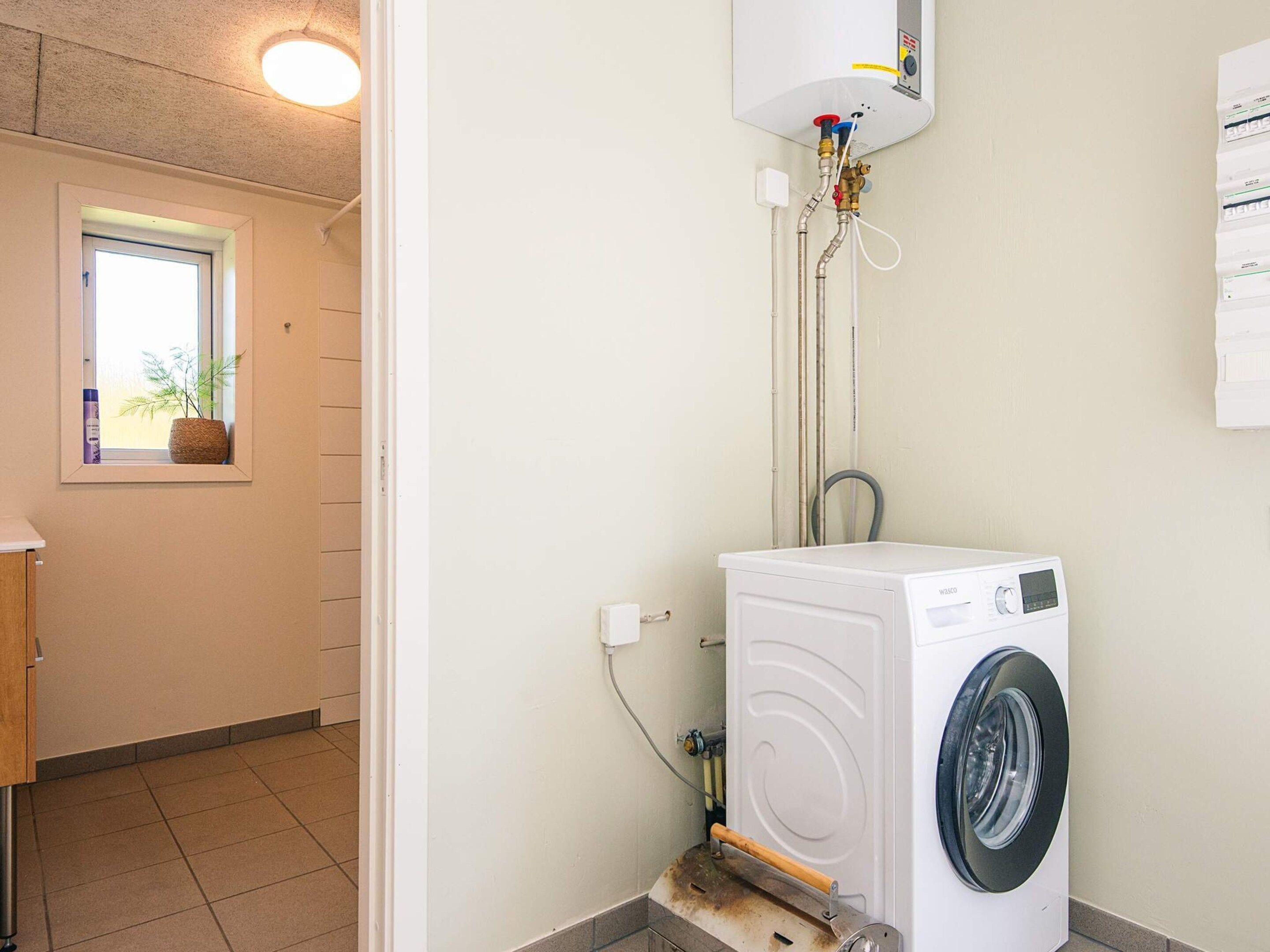 Une buanderie équipée d’un lave-linge à chargement frontal, d’un chauffe-eau et d’une fenêtre agrémentée d’une plante.