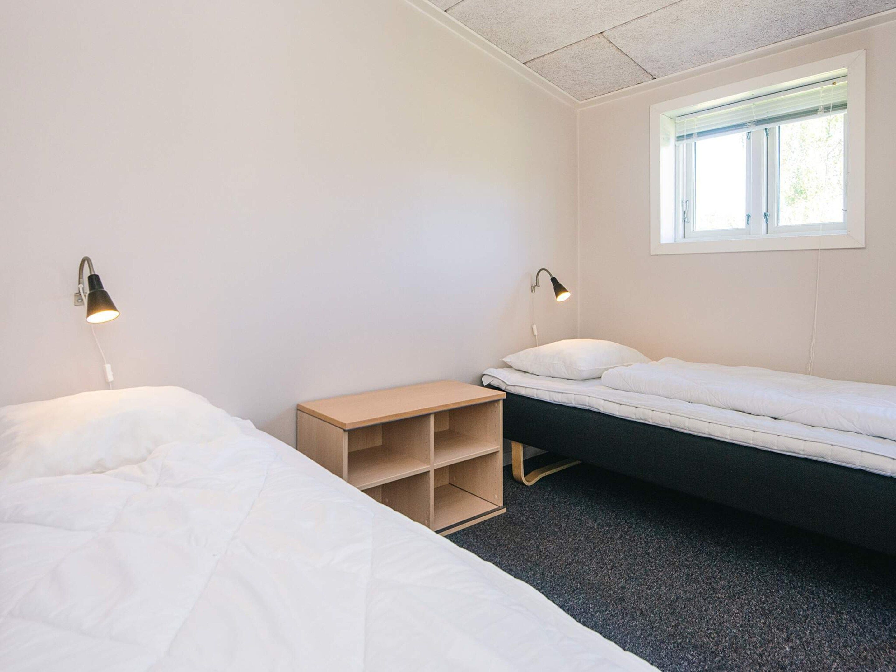 A simple, clean room with two beds, a small wooden nightstand, and two wall-mounted reading lamps.