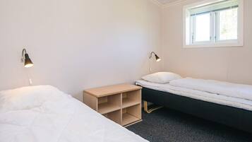 A simple, clean room with two beds, a small wooden nightstand, and two wall-mounted reading lamps.