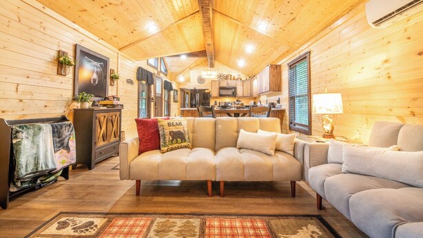 A cozy cabin interior with a sofa, a dining area, and a kitchen. - 🔥 Tennessee Dream | Cozy Retreat with Fire Pit + Mortal Kombat Arcade🌲 (Sevierville)