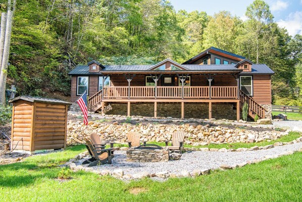 A cabin with a wooden exterior, a deck, and a stone fire pit.