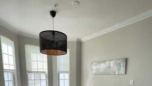 Un coin repas comprenant une table en verre, quatre chaises, un luminaire suspendu noir et un tapis gris.
