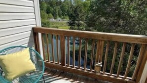 Un balcon avec une balustrade en bois, une petite table blanche et une chaise verte avec un coussin jaune.
