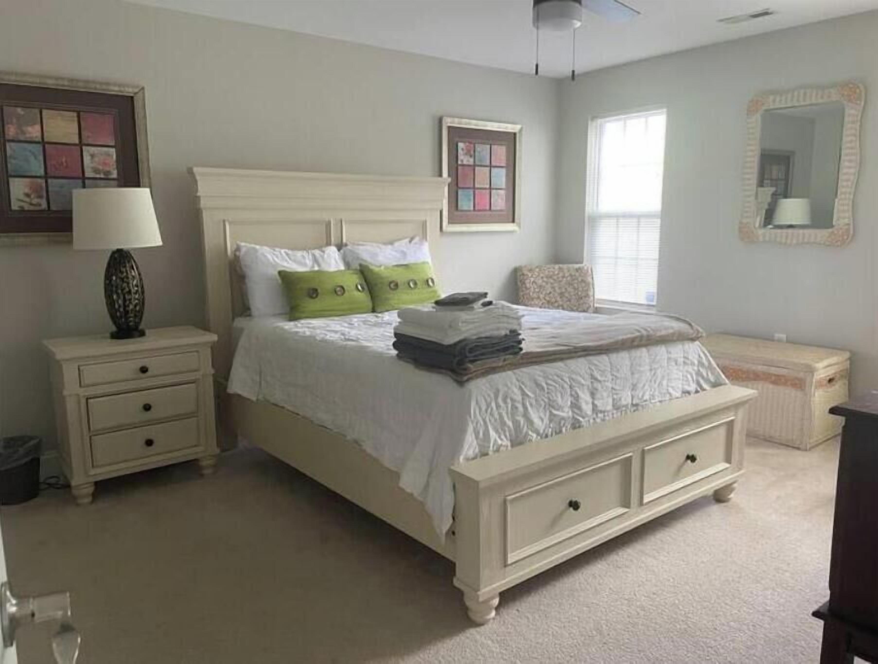 A bedroom with a bed, a nightstand, a dresser, a mirror, and a window.