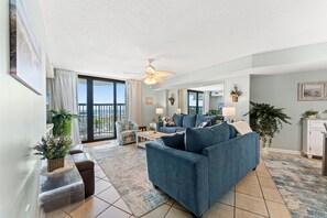 A spacious living room with a blue sofa, a coffee table, and a balcony with a view. - Ocean Bay Club 102 4BR OF Condo Close to Main St (North Myrtle Beach)