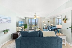 A living room with a blue sofa, a television, and a view of the ocean through large windows.