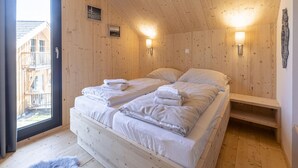 A wooden room with a bed, two wall-mounted lights, a window, and a view of buildings outside. - Inviting Chalet With Terrace (Sankt Georgen am Kreischberg)