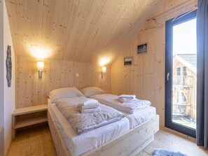 Ein Schlafzimmer einer Holzhütte mit zwei Betten, einer Bank und einem Fenster mit Blick ins Freie.