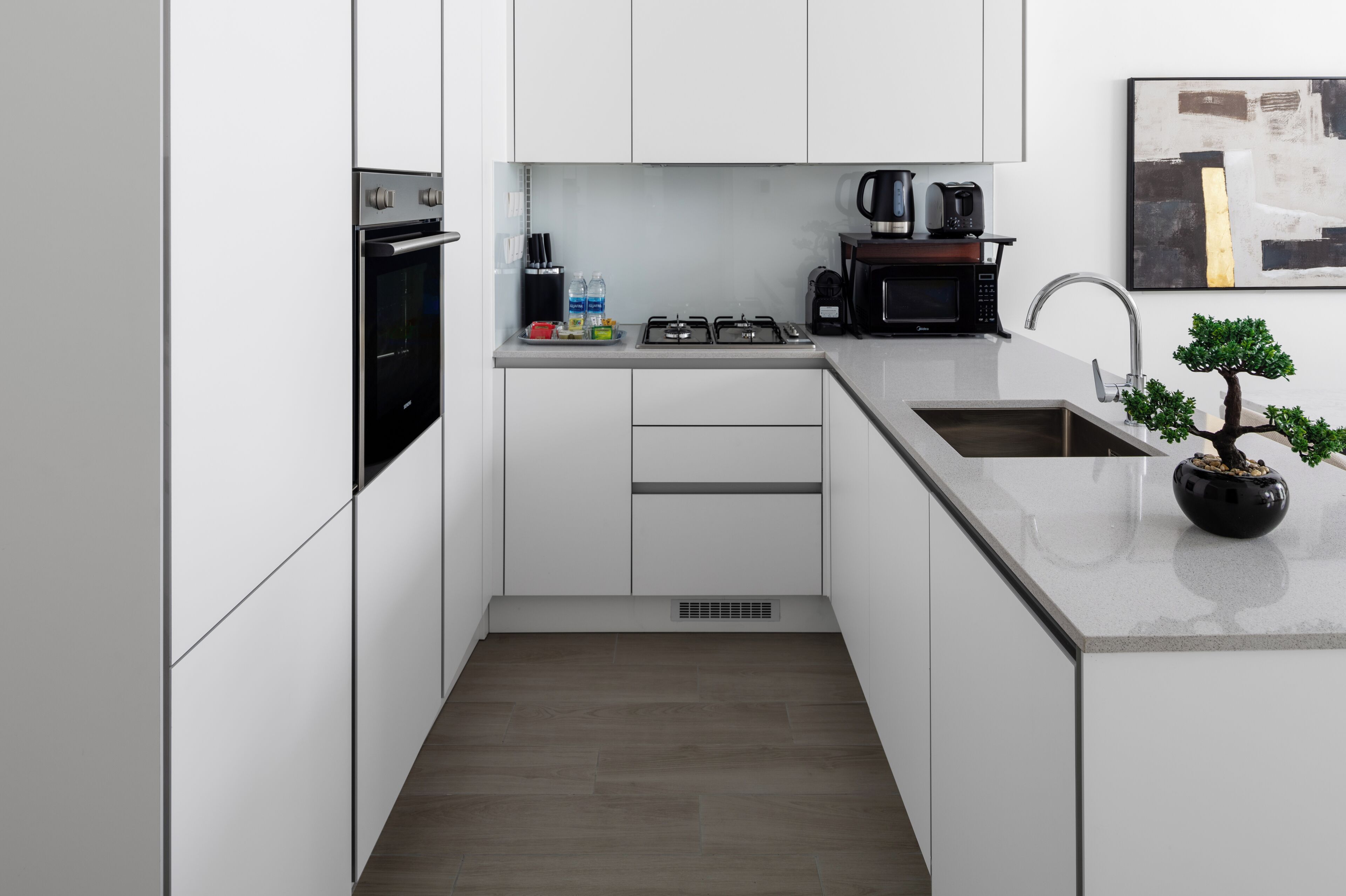 A modern kitchen with white cabinets, a built-in oven, a microwave, and a sink.