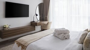 Une chambre d’hôtel moderne dotée d’un grand lit, d’un téléviseur à écran plat fixé au mur, d’une console en bois et d’une grande fenêtre avec des rideaux légers.
