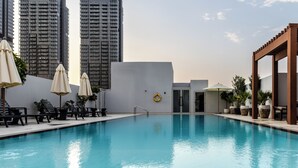 Une piscine entourée d’immeubles imposants, avec des chaises longues et des parasols.