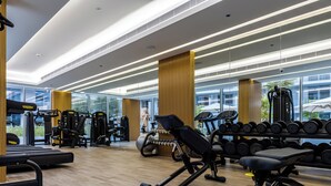 Une salle de sport moderne équipée de divers appareils d’exercice, dotée de grandes fenêtres et d’un plancher en bois.