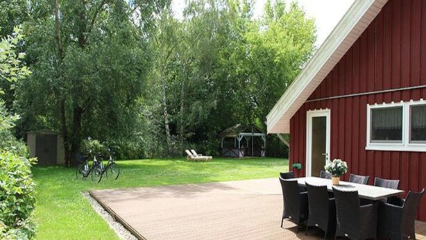 Un bâtiment rouge doté d’une terrasse en bois, de sièges en plein air et d’une pelouse.