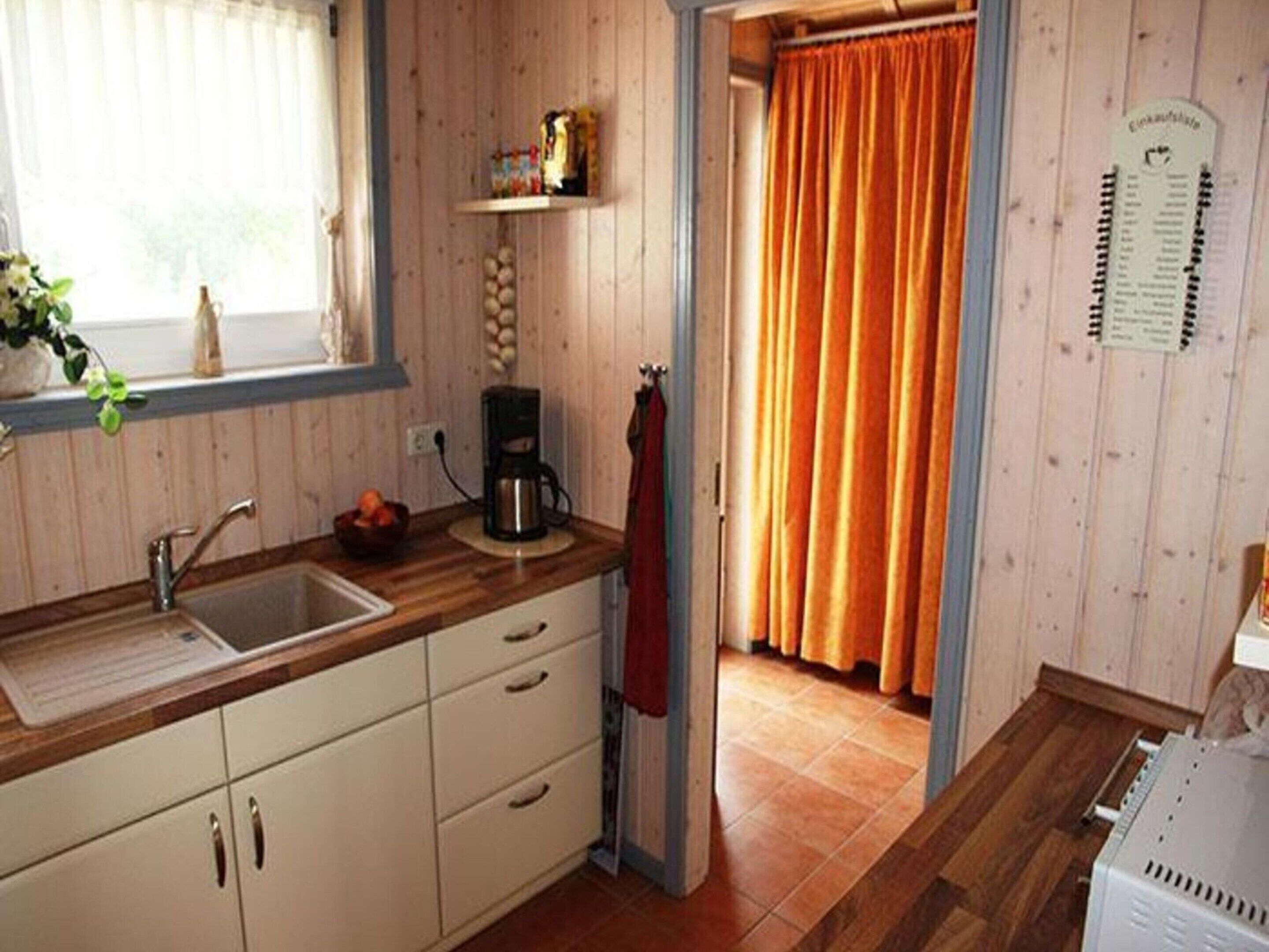 A kitchen with wooden cabinets, a sink, a coffee maker, and a window with curtains.