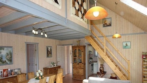 Ein geräumiger Wohnbereich mit einem Esstisch, Holzsesseln, einem grauen Sofa und einer Treppe.