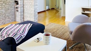 Una sala de estar acogedora con pared de ladrillo, sofá azul, una mesa blanca con una taza y un sillón gris.