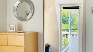 Una habitación con un aparador de madera, un espejo redondo y una puerta que da a un balcón con barandilla de madera.