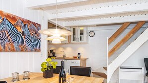 A modern kitchen with white cabinets, a dining area with a wooden table, and a staircase leading to another level.