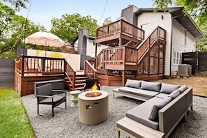 Un jardin avec un foyer extérieur, des meubles de jardin, une terrasse en bois et un escalier menant à un balcon situé à l’étage.