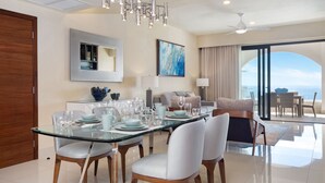 A modern dining area with a glass table, white chairs, and a chandelier. There is a sofa and a balcony with a view. - Amazing 1 bedroom condo, ocean view with AC in San José del Cabo (San José del Cabo)