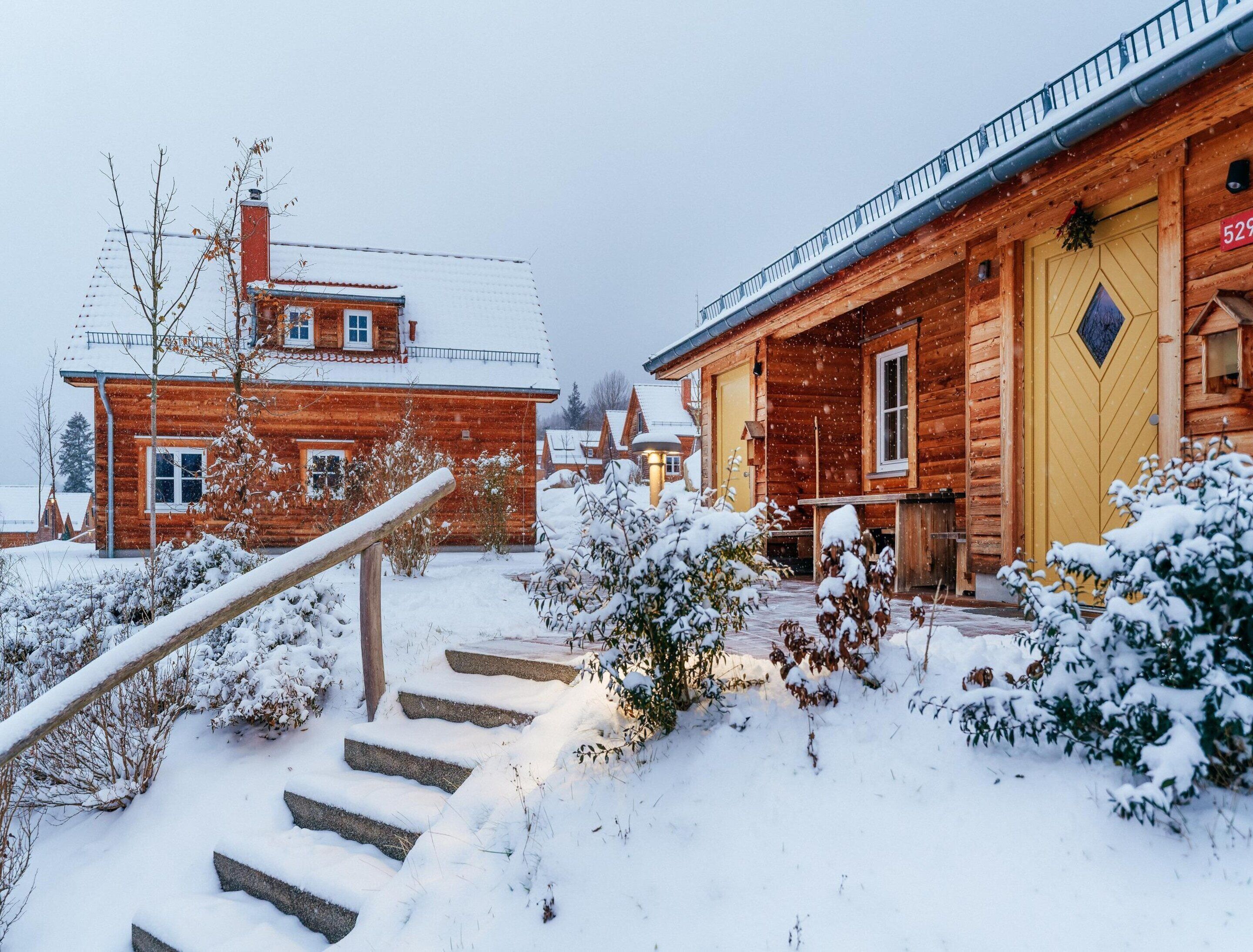 A wooden cabin with a snow-covered roof and steps leading to the entrance.