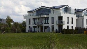 A modern two-story house with large windows and balconies, surrounded by a grassy field. - Appartementhaus Calmsailing, Borgerende (Boergerende-Rethwisch)