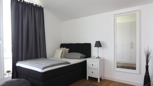 A bedroom with a bed, bedside table, lamp, and a mirror. - Appartementhaus Calmsailing, Borgerende (Boergerende-Rethwisch)