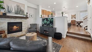 Een woonkamer met een open haard, een televisie, een bank en een eethoek met een tafel en stoelen.